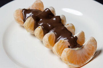 Tangerine slices in chocolate on a white plate. Peeled tangerine topped with melted chocolate. Fruit dessert