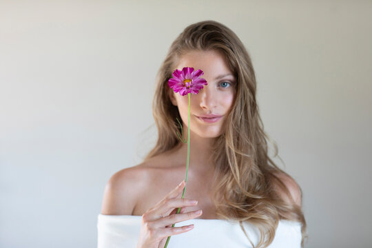 Young woman in off shoulder top covering eye with purple daisy