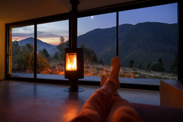 Woman resting near fireplace at modern house with great view on mountains at sunset. Women's legs...