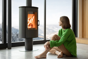 Woman sitting near fireplace at modern living room with stunning view on snowy mountains. Concept...