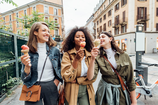 Smiling friends having ice cream while walking in city