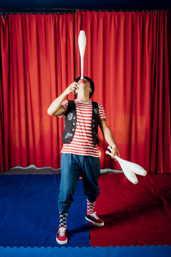 Male clown balancing juggling pin on nose in circus