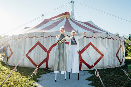 Female artists playing accordion while standing on stilts by male circus performer