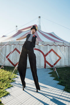 Male artist balancing on stilts in front of circus tent