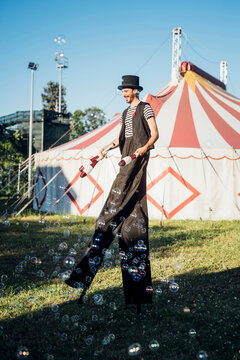 Male juggler holding juggling pins while walking with stilts on meadow