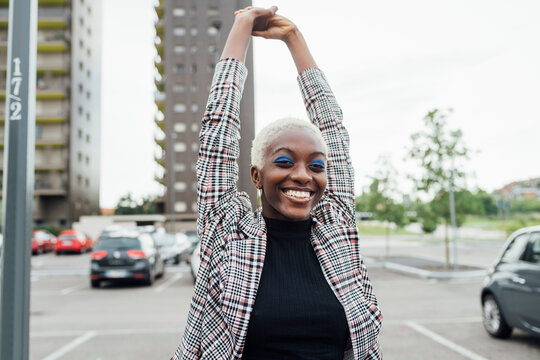 Smiling woman standing with hands raised on road
