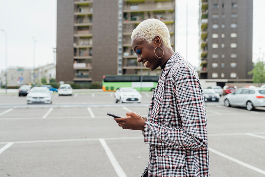 Smiling woman using mobile phone while working at parking lot