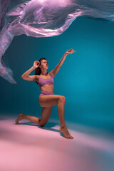 One young flexible contemp dancer dancing with fabric isolated on gradient blue white background in neon light