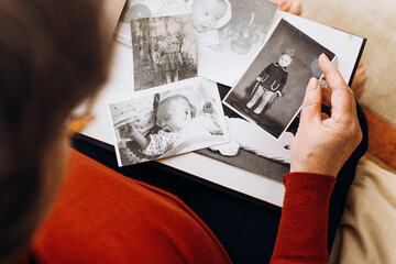 An elderly woman holding album with black and white retro photographs of childhood, remembering...
