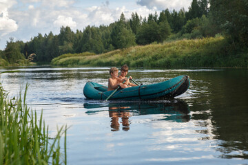 Fototapeta na wymiar Two children ride a rubber boat on the river on a summer day.