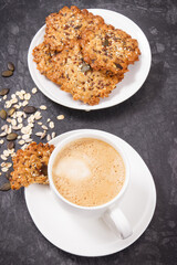 Cup of coffee with milk and homemade oatmeal cookies on white plate. Delicious crunchy dessert