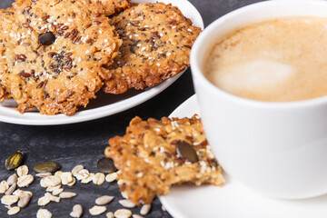 Cup of coffee with milk and fresh baked oatmeal cookies with honey and healthy seeds. Delicious crunchy dessert