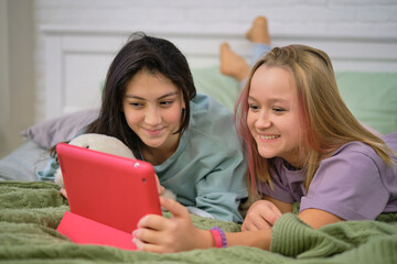 Two teen girls sit at the laptop and look at the monitor chatting with friends over video chat.