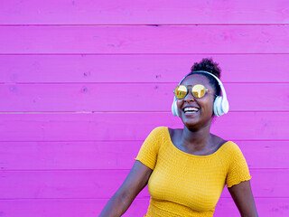 african woman dancing and smiling, pink background in contrast with yellow clothes and jeans, afro...