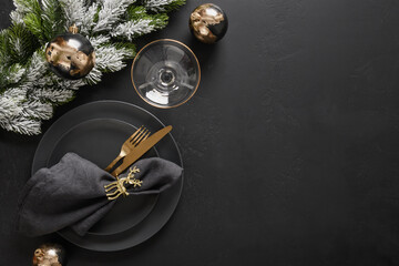 Luxury New Year and Christmas table setting with black plates, champagne flutes, gold deer ring and gold cutlery on black background with copy space. View from above.