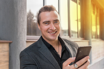 Portrait of a smiling, cheerful man of Caucasian appearance of a businessman in a jacket and shirt with a mobile phone in his hands on the street outdoor