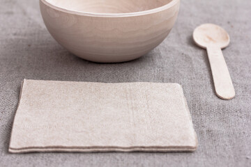 Eco-friendly disposable biodegradable brown napkin made from recycled paper, a wooden bowl and a wooden  bamboo spoon on brown background. Alternative to plastic single use