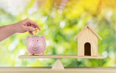 wooden home and piggy bank with hand hold gold coin Us dollar sign put on the scales with balance...
