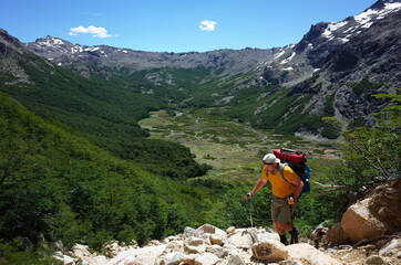 Trekking in Patagonia, Man with big backpack walking up on mountainside with view of green Rucaco...