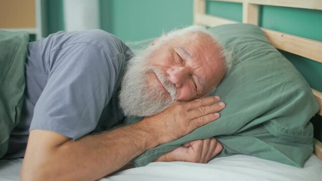 Portrait of an Elderly Man Sleeping Quietly on a Bed in His Room. Happy Retired Man Smiling, Lying in Bed, Sleeping on a Comfortable Mattress And Pillow, Resting Peacefully. Healthy Sleep Concept.