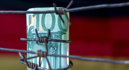 The global economic recession and crisis of European Union. EURO banknotes wrapped in barbed wire against flag of Germany. Copy space for design.