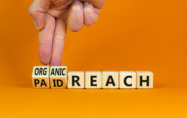 Organic or paid reach symbol. Businessman turns wooden cubes and changes words paid reach to organic reach. Beautiful orange table orange background copy space. Business organic or paid reach concept.