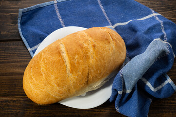 fresh baked loaves of bread on lie on a dark wooden table next to a blue towel rag