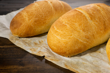 fresh baked loaves of bread on lie on a dark wooden table next to a blue towel rag