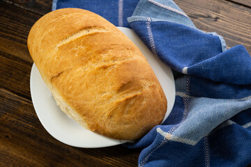 fresh baked loaves of bread on lie on a dark wooden table next to a blue towel rag