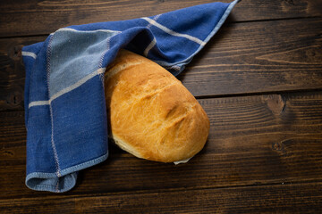fresh baked loaves of bread on lie on a dark wooden table next to a blue towel rag