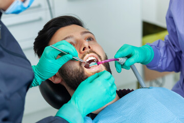 Female dentist examines a man patient in a dental office using professional tools and personal protective equipment.
