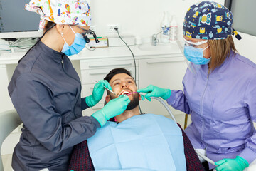 Female dentist examines a man patient in a dental office using professional tools and personal protective equipment.