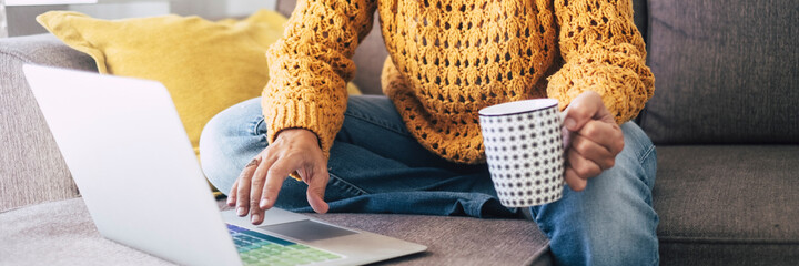 Banner header modern woman at work writing on laptop computer at home sitting on the sofa and drinking a coffee
