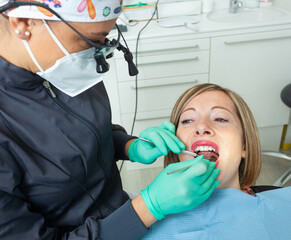 Young Blonde Female patient with open mouth examining dental inspection at dentist office.