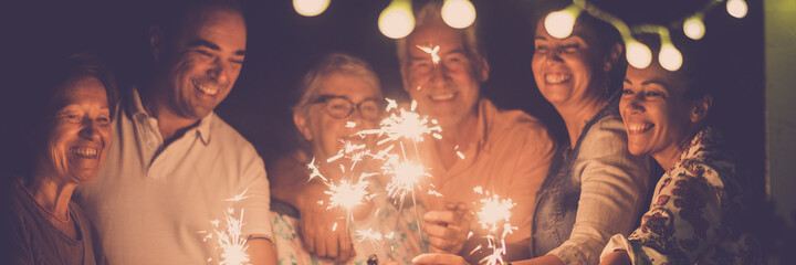 Group of people celebrate with sparkler in friendship. Family with men and women have fun in the night celebrating new year or birthday in banner header size image