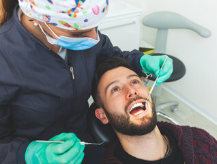 Female dentist examines a man patient in a dental office using professional tools and personal...