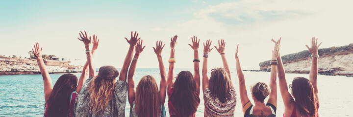 Group of women viewed from back with arms up for happiness in front of blue sea ocean water. Vacation and joyful people banner © simona