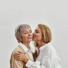 Loving grownup daughter kiss mature mom in cheek - obrazy, fototapety, plakaty