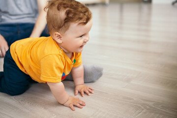 Little boy smiling cheerfully cute child redhead laughing baby learning crawling playing on the floor. Toddler having fun at home dressed orange t-shirt. Happy childhood, family concept
