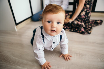 Little boy smiling cheerfully cute child redhead laughing baby learning crawling playing on the floor. Toddler having fun at home dressed overalls suspenders and white shirt. Happy childhood
