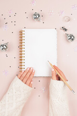 A blank notepad next to Christmas decor. Woman is writing New Year resolution, wish list, goals, diary, thoughts and dreams. Journaling concept. Flatlay, top view.