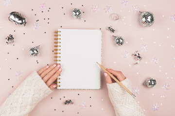 A blank notepad next to Christmas decor. Woman is writing New Year resolution, wish list, goals, diary, thoughts and dreams. Journaling concept. Flatlay, top view.
