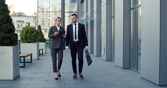 Two young caucasian handsome businesspeople walking together in the city center near the office center and having a nice talk