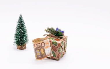 A gift box decorated with a fir branch, a 50 euro paper bill and a Christmas tree on a white background. The concept of gifts and surprises for the Christmas holidays.