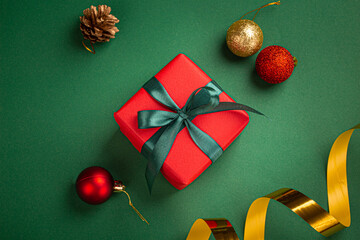 Christmas present box wrapped in red paper with green ribbon and bow, Christmas sparkly round balls decorations on green paper background top view, Christmas composition in red, green and golden