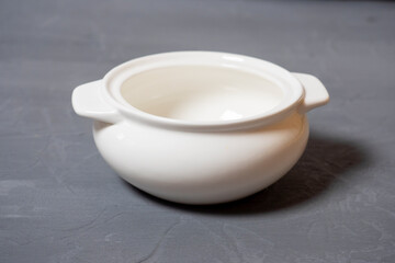 Close-up of an empty tureen made of white porcelain standing on a textured gray background. Dishes for food. Side view, selective focus