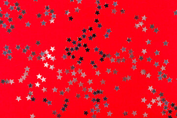Festive Christmas and New Year background. Silver stars confetti on a red background top view