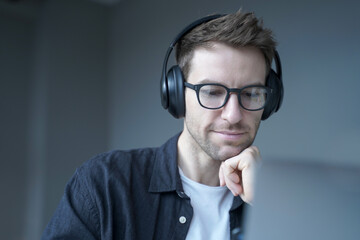 Smiling german man in headphones looking on screen of laptop and watching educational webinar
