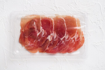 Vacuum pack of sliced prosciutto, on white stone table background, top view flat lay, with copy space for text