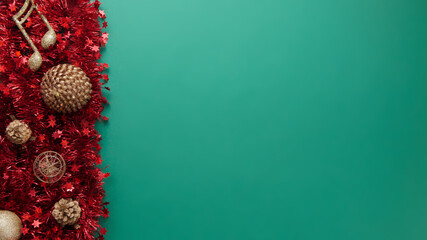 Flat lay of red and gold Christmas decoration on the left side of a green background. Golden balls...
